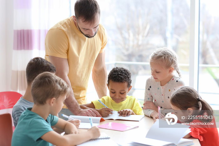 Male teacher helping children with homework in classroom at school