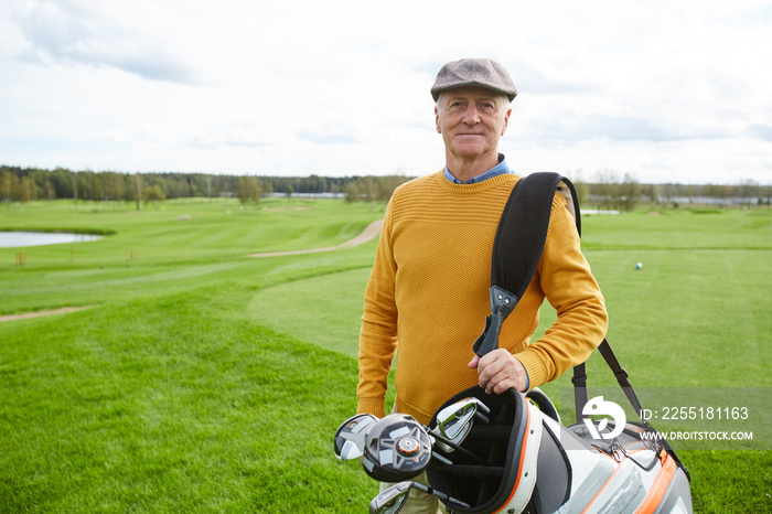 Aged successful golf player with bunch of clubs in sportive bag on his shoulder looking at you