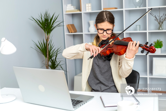 Girl student learns to play the violin online using a laptop.