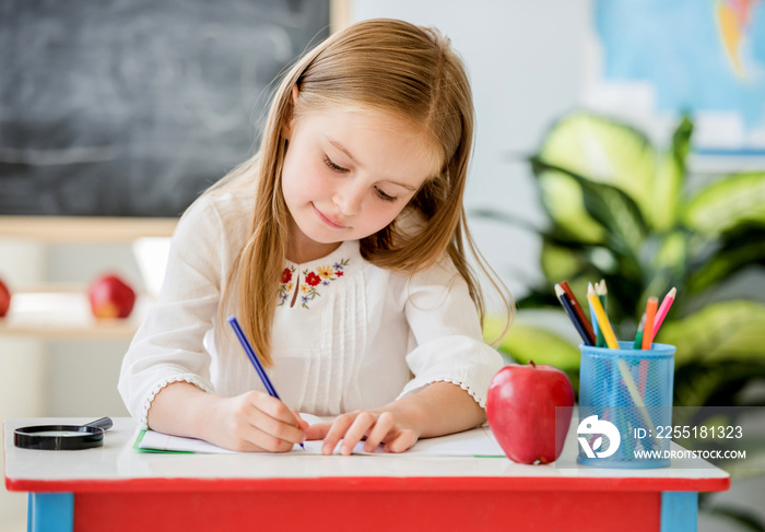 Little blond girl writing classwork in the school classroom