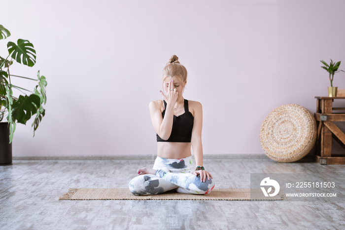 Front view portrait of young woman working out, resting after doing yoga exercises, using nadi shodhana pranayama technique ana breath