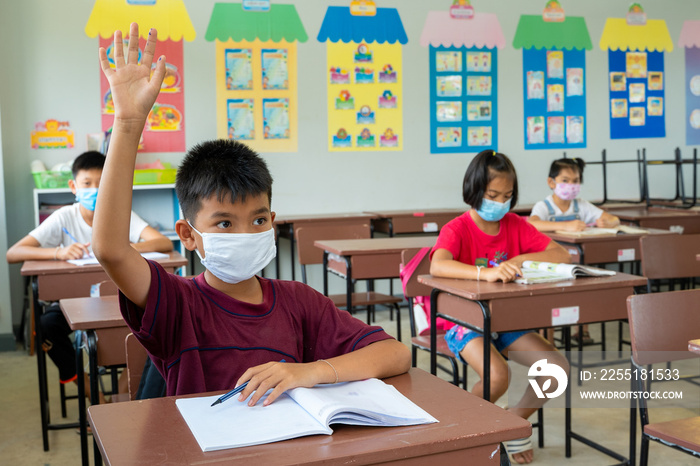 School kids wearing protective mask to Protect Against Covid-19,Group of school kids with teacher sitting in classroom and raising hands,Elementary school,Learning and people concept.