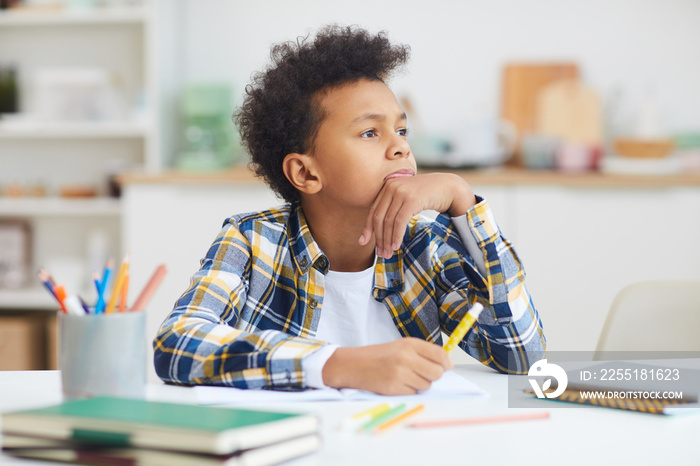 Portrait of teenage African-American boy daydreaming at desk while doing homework, copy space