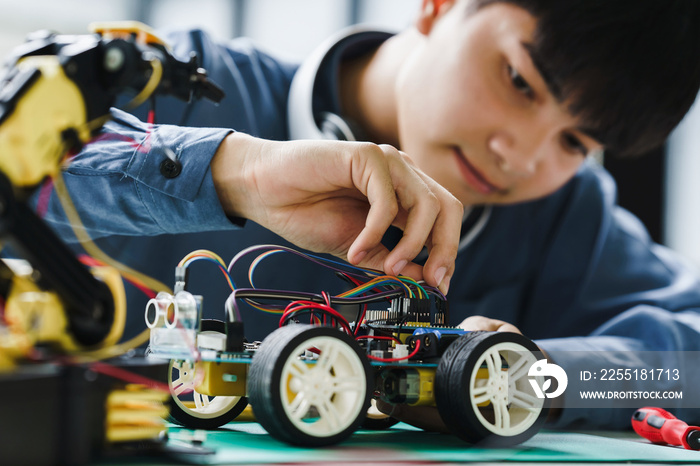 Asian teenager students doing robot arm and robotic cars homework project in house disassemble the circuit and coding. technology of robotics programing and STEM education concept.