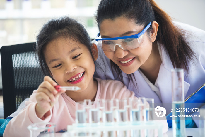 little asian children girl in elementary science class doing chemical experiment helped by woman teacher test, experimen, try drop color water to plate. Education science workshop concept.