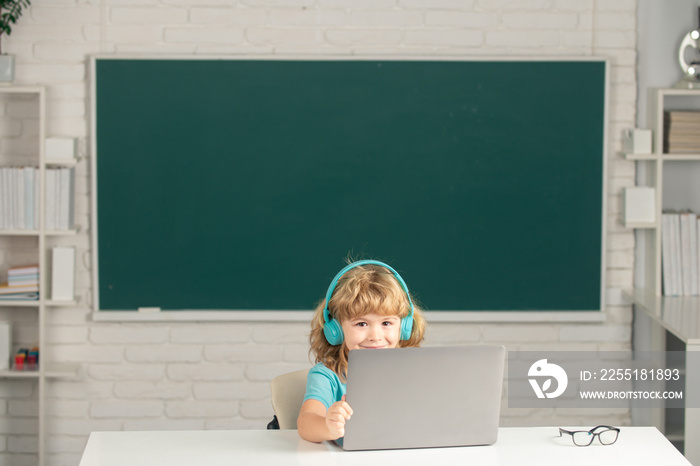 Child boy in headphones using a laptop and study online with video call teacher at school. Elementary school and education.