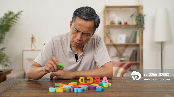 asian senior male with dementia trying to recognize and arrange color letter blocks in order at home. in-home care and brain exercise for rehabilitation concept