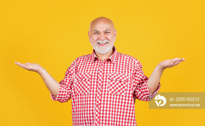 happy old man in checkered shirt presenting product on yellow background