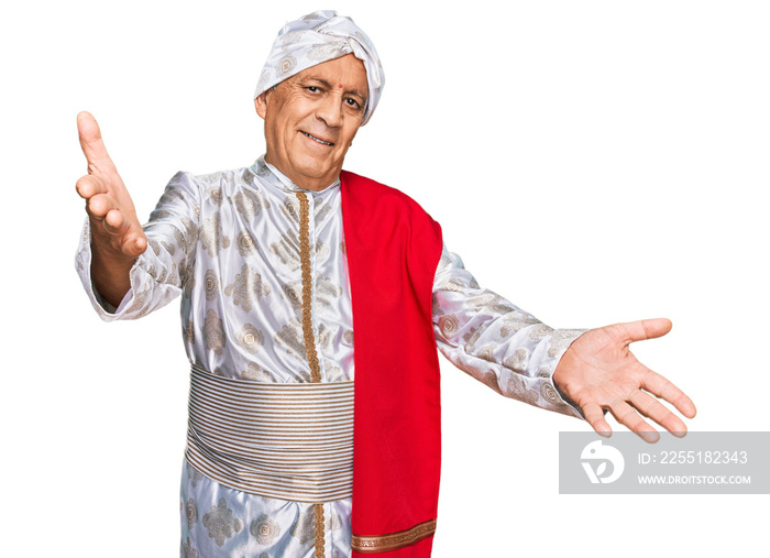 Senior hispanic man wearing tradition sherwani saree clothes looking at the camera smiling with open arms for hug. cheerful expression embracing happiness.