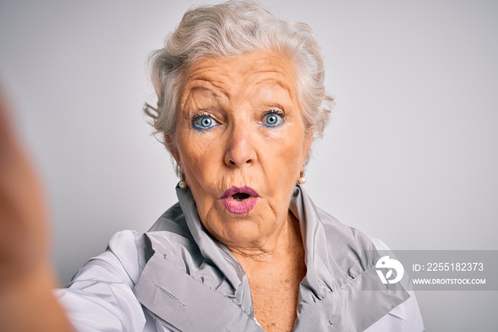 Senior beautiful grey-haired woman making selfie by camera over isolated white background scared in shock with a surprise face, afraid and excited with fear expression