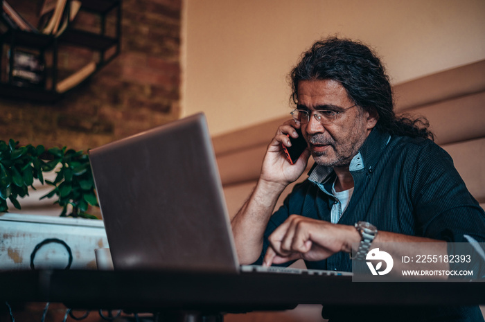 Senior hispanic cuban men using smartphone while working on his laptop in a cafe