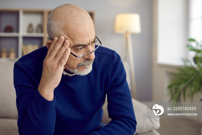 Older man with serious and thoughtful expression looks away thinking about something important. Close up head shot of man with glasses holding hand near his head. Old age, problem and people concept.