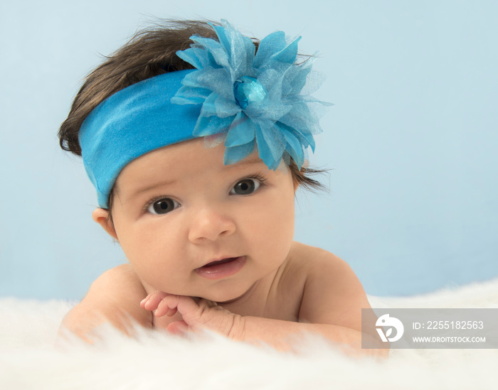 Two month old girl in blue headband on white fur, looking at camera