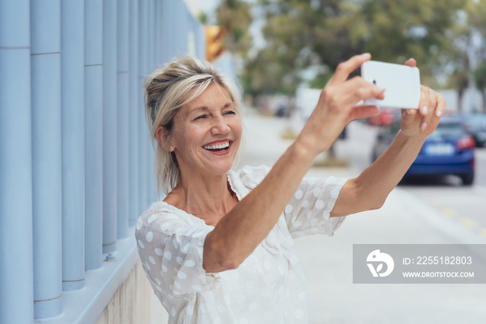 Cheerful mature woman talking selfie on smartphone