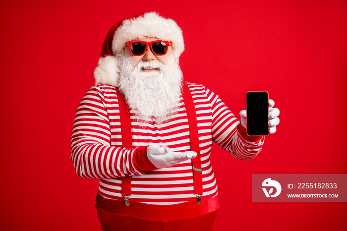 Portrait of his he nice handsome cheerful bearded fat Santa holding in hand demonstrating novelty gift present surprise gadget isolated on bright vivid shine vibrant red color background