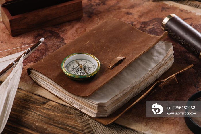 brown leather notebook with compass on wooden surface with world map