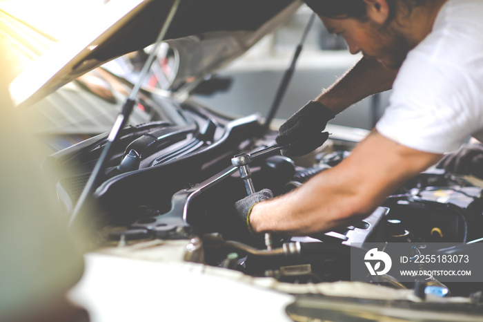 Caucasian male mechanic repairs car in garage. Car maintenance and auto service garage concept. Closeup hand and spanner.