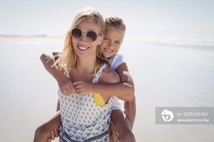 Happy mother piggybacking her daughter at beach