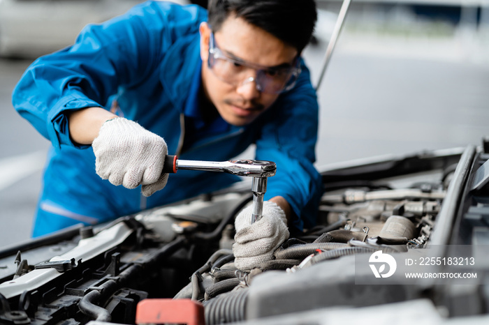 Close-up of a car mechanic repairing a car in a garage, car safety check The engine in the garage, Repair service concept. Asian mechanic in blue uniform working at the repair garage,