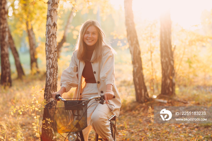 Happy active young woman riding vintage bicycle in autumn park at sunset