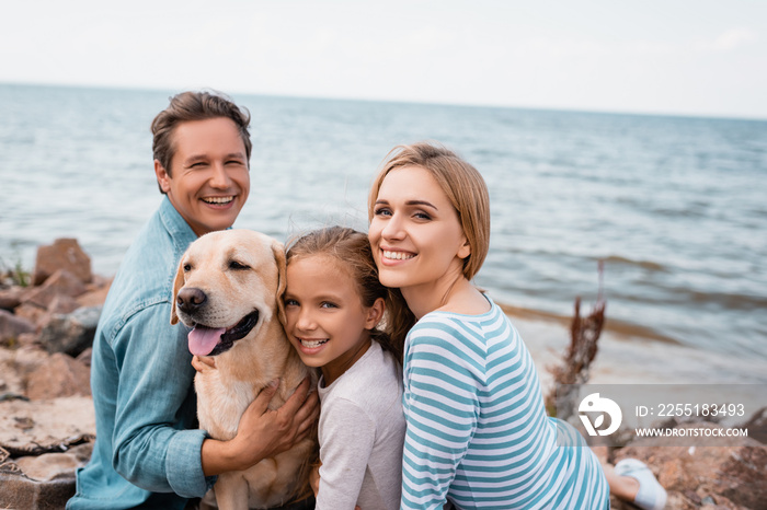 Family with child and golden retriever looking at camera during weekend on beach