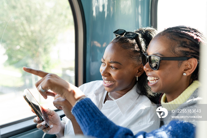 Young female friends riding city bus and using phone