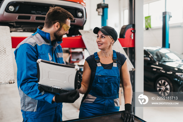 Male and female mechanics working together in large modern car repair service.