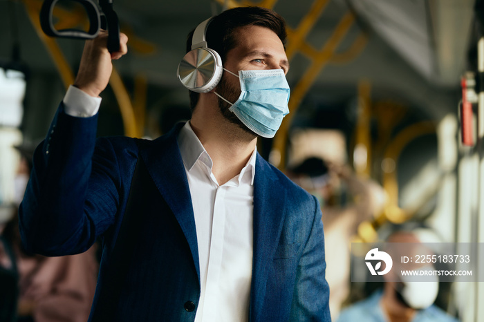 Businessman with face mask listening music over headphones while commuting by public transport.