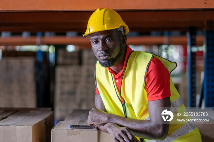 Africa American engineer man wearing safety helmet and vest standing in the automotive part warehouse. Looking at camera Portrait of worker. Logistic and business export at distribution center