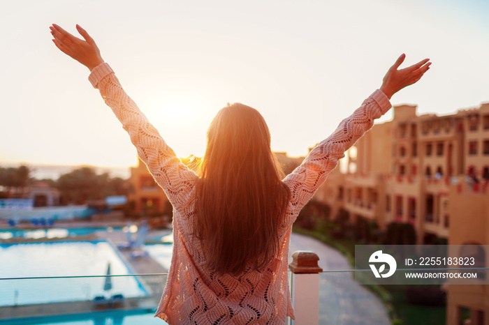 Woman relaxing at hotel balcony enjoying sunrise with swimming pool and sea view.