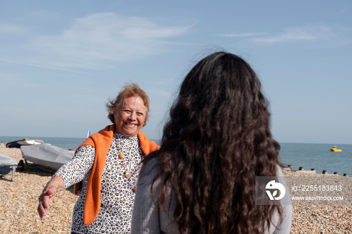 Mother and daughter greeting on beach on sunny day