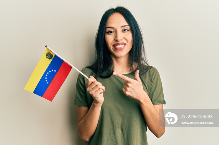 Young hispanic girl holding venezuelan flag smiling happy pointing with hand and finger