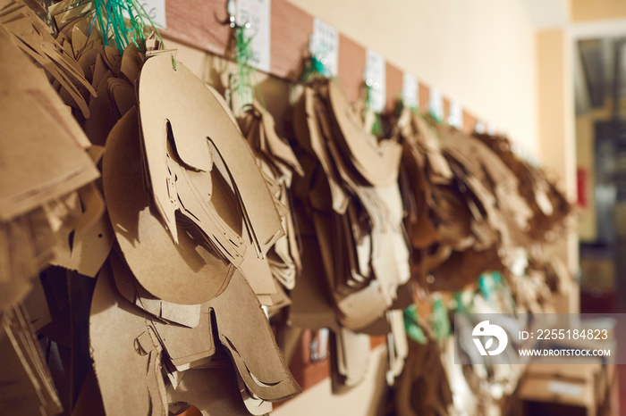 Closeup shot of different paper sewing patterns for original brand leather boots hanging on wooden peg rack in manufacturing workshop at shoe making factory. Footwear production industry concept