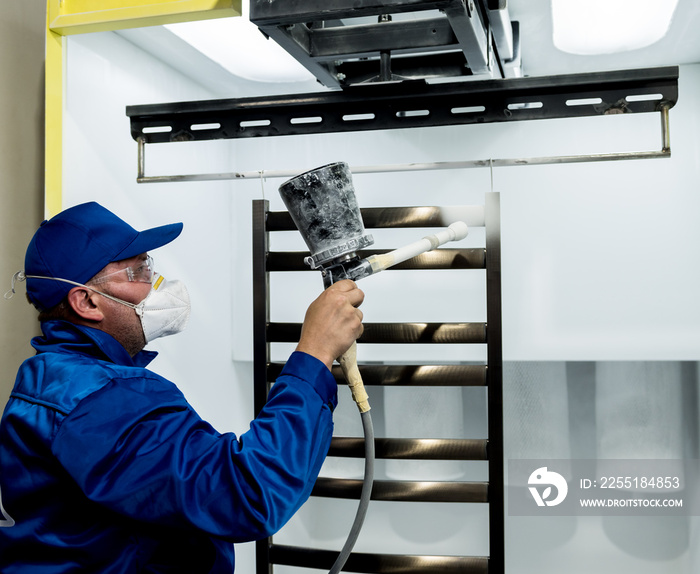 Worker performing powder coating of metal details at metallurgical factory