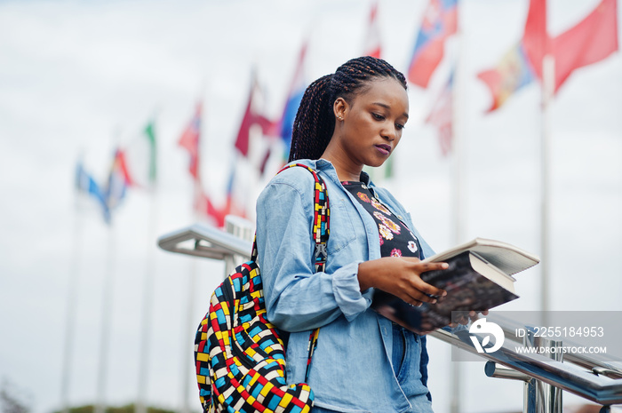 African student female posed with backpack and school items on yard of university, against flags of different countries.