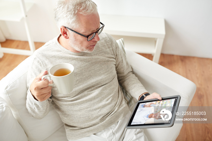 medicine, technology and healthcare concept - senior man having video chat with pharmacist on tablet pc computer and drinking tea at home