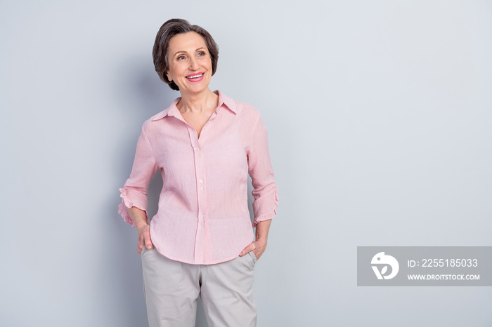 Photo of charming pretty age woman dressed pink shirt smiling arms pockets looking empty space isolated grey color background