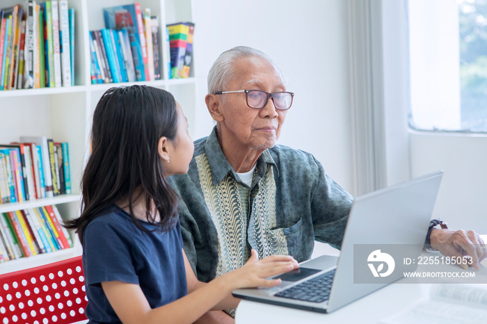 Senior man teaches his grandchild to use a laptop