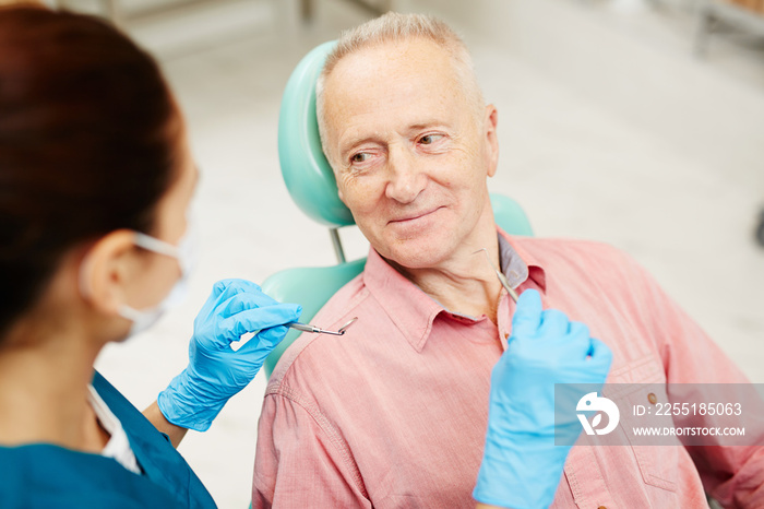 Mature man looking at his dentist with check-up tools during consultation