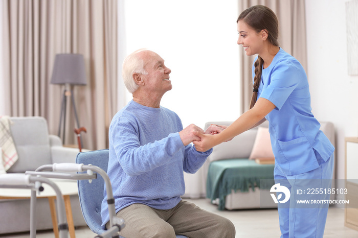 Senior man and young caregiver holding hands indoors