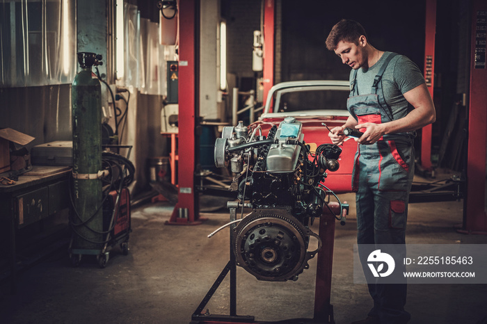 Mechanic working on classic car engine in restoration workshop