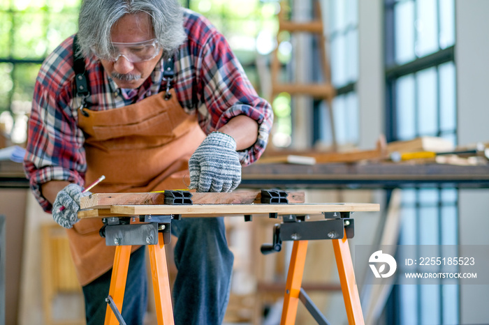 Senior or Old Asian craftsman act as measurement of wood in the room with wood pile and surround with glasses.