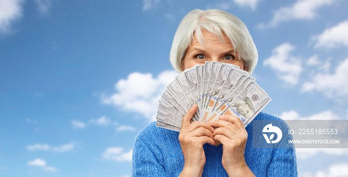 savings, finances and people concept - smiling senior woman hiding face behind hundreds of dollar money banknotes over blue sky and clouds background