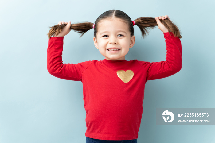 Gorgeous little three year old girl holding up her ponytails and smiling in a studio