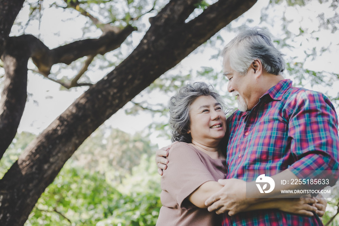 Happy senior couple Grandfather and grandmother embracing each other with love and smiley faces under tree at park. Elderly husband hug old wife and enjoy life with happiness Health care and insurance