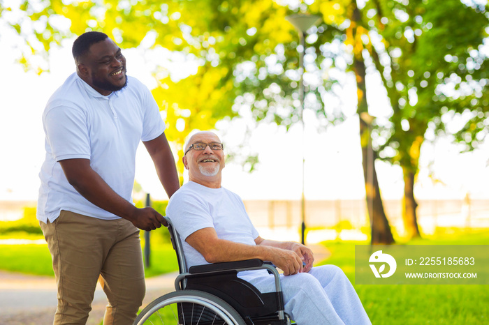 Caregiver and old man in a wheelchair. Professional nurse and patient walking outdoor in the park at sunset. Assistance, rehabilitation and health care.