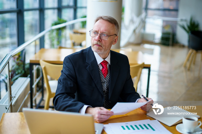 Content senior business man sitting in a dark suit. Documents in hands. Red tie. Confident. Business style concept