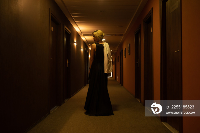 Luxury girl in black dress at night in the hotel corridor.