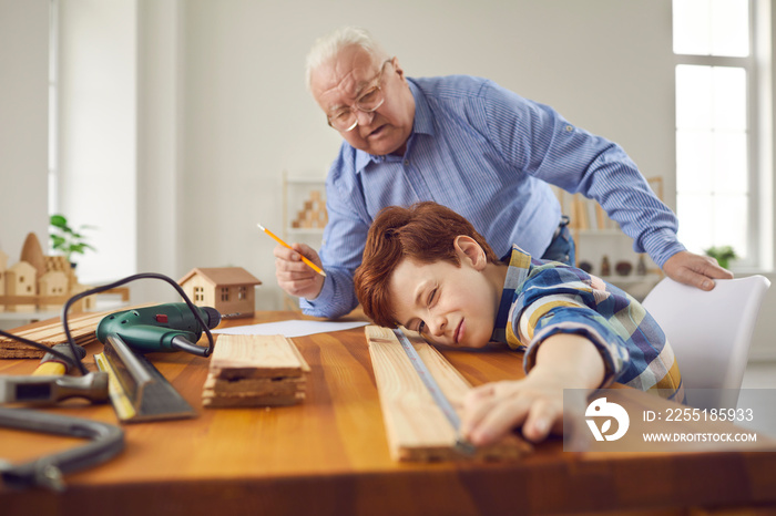 Grandfather and grandson fixing things in workshop. Skillful carpenter teaching little child new handwork skills. Old man with teen boy measuring wood plank to make wooden toys or do home repairs