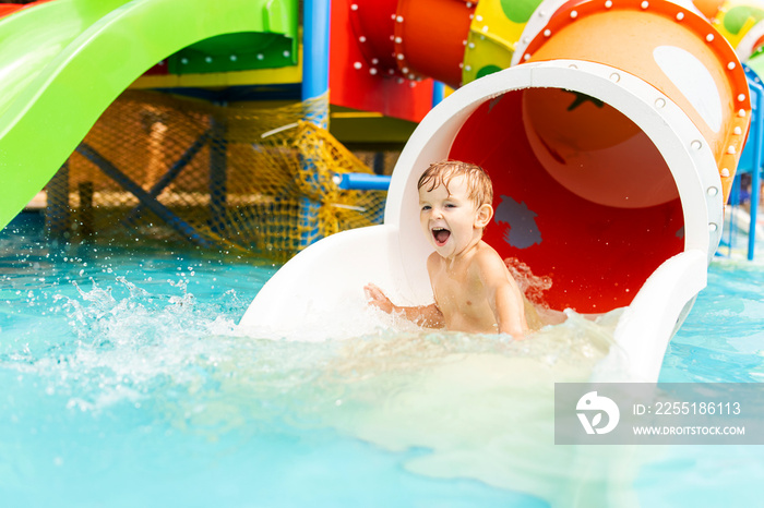 Little boy playing on water slide in outdoor pool on a hot summer day